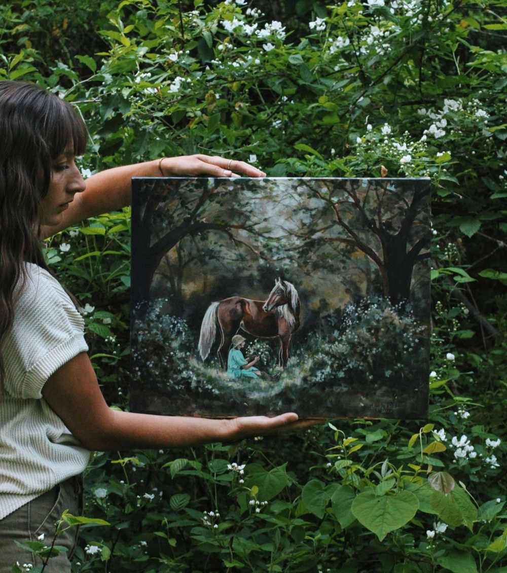 Featured artist Amelia Polder holding one of her paintings in her garden