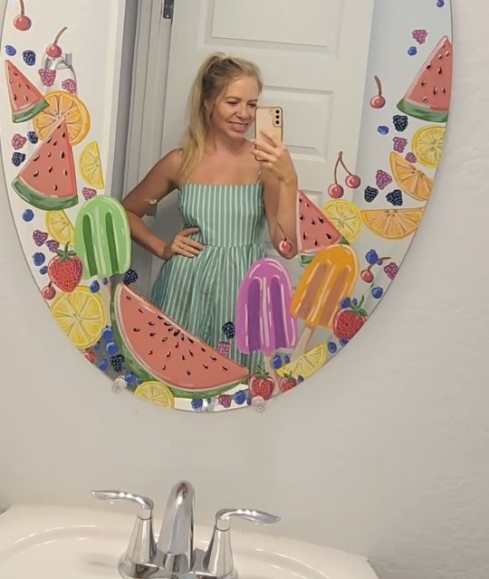 Rebecca in front of her bathroom mirror, hand-painted with watermelon, citrus and popsicles for summer