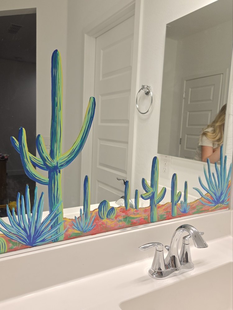 A mirror hand-painted with blue saguaro cacti and desert plants