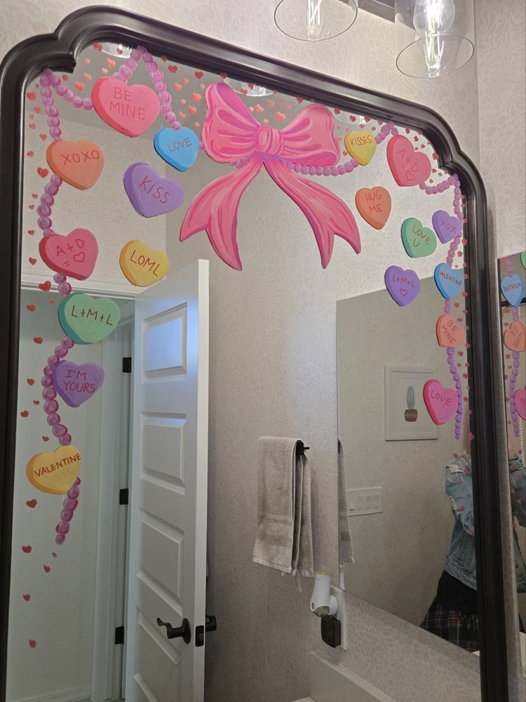 A mirror hand-painted with Valentine's conversation hearts and a pink bow